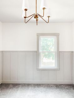 an empty room with white walls and wood paneling on the wall, along with a window