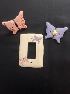 three ceramic butterflies are sitting next to a white light switch plate on a black surface