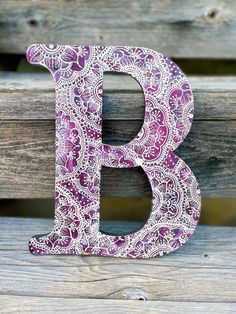 the letter b is decorated with purple paisley fabric and sits on a wooden bench in front of a fence