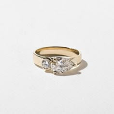 a yellow gold ring with two pear shaped diamonds on the side, set against a plain white background