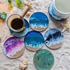 six coasters with different designs on them sitting in the sand next to a cup of coffee