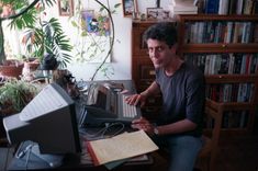 a man sitting in front of a computer on top of a desk next to a plant