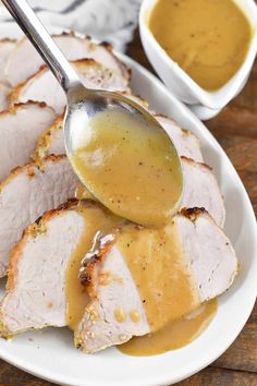 a white plate topped with sliced pork covered in gravy and a spoon full of gravy