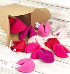 pink and red felt hearts are in a cardboard box on a white wooden surface with love tag