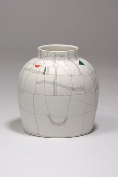 a white vase with lines painted on the side and an orange dot in the middle