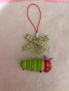 a green and red caterpillar ornament hanging on a white blanket with a ribbon