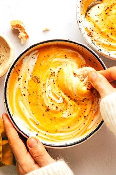 two bowls filled with hummus and sauce on top of a white table next to other dishes