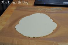 an uncooked pizza sitting on top of a wooden table next to a laptop