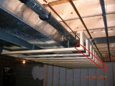 an unfinished room with exposed pipes and wood beams on the ceiling, below which is a red arrow pointing up