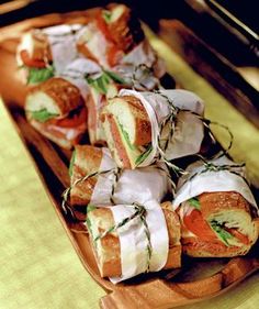 many sandwiches are wrapped in white paper on a wooden platter