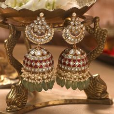 a pair of red and green earrings sitting on top of a gold plated stand