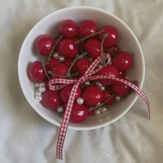 a white bowl filled with cherries tied in a red ribbon on top of a bed