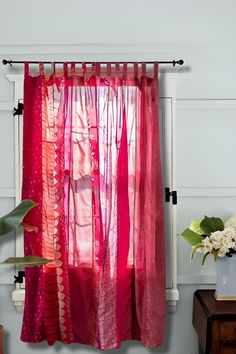 a pink curtain hanging from the side of a window next to a potted plant