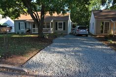 a car parked in front of a house next to a gravel driveway with trees on both sides