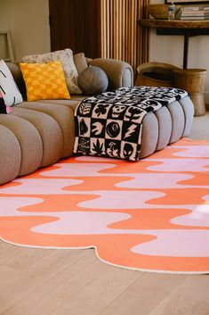 an orange and black rug on the floor in front of a couch with various pillows