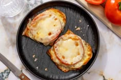 two pieces of bread topped with cheese and sauce on a plate next to sliced tomatoes