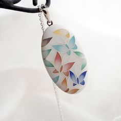 a white necklace with multicolored leaves is hanging from a black chain on a white background