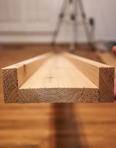 a person holding a piece of wood on top of a hard wood floor in front of a camera