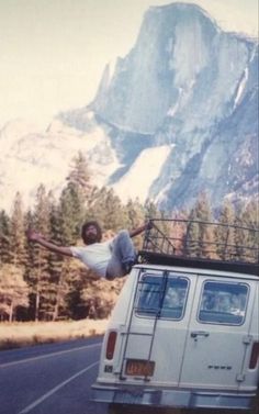 a man is jumping off the roof of a van in front of a mountain range