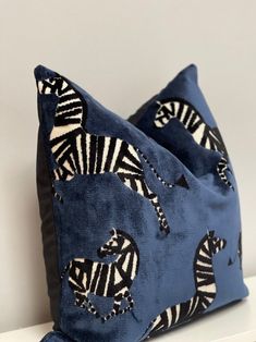 two blue pillows with zebras on them sitting on a white shelf next to each other