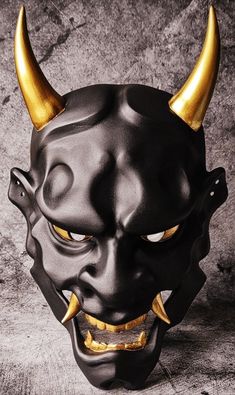 a black mask with gold horns and fangs on it's face, against a gray background