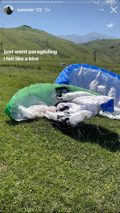 an umbrella laying on top of a lush green field next to a hill with mountains in the background