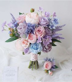 a bridal bouquet with pink, blue and purple flowers on a white cloth background