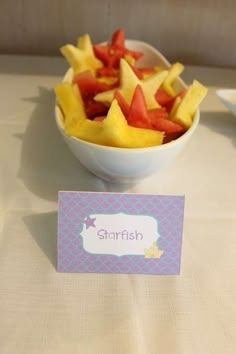 a bowl filled with cut up fruit on top of a table next to a place card