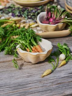 carrots, radishes and other vegetables on a wooden table with bowls full of them