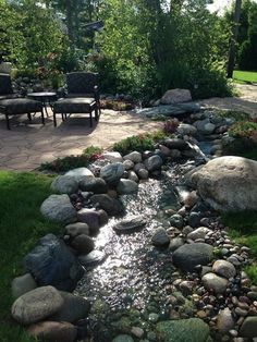 a small stream running through a lush green yard next to a stone patio and table