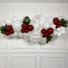 white and red balloons are hanging on the wall with greenery, holly leaves and berries