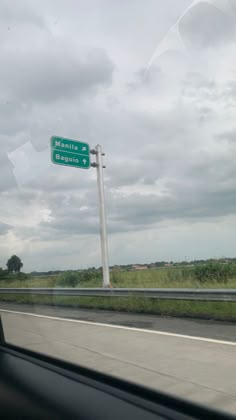 a green street sign sitting on the side of a road next to a lush green field