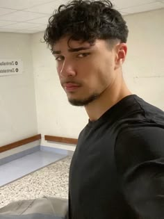 a young man with curly hair is looking at his cell phone in an empty room