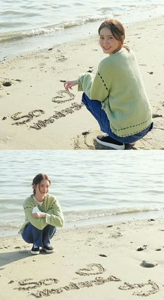 a woman kneeling on top of a sandy beach next to the ocean and writing in the sand