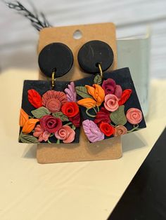 the earrings are decorated with flowers and black disc shaped earwires on top of a cardboard box