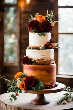 a three tiered cake with red and orange flowers on top is sitting on a wooden table