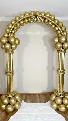 an arch made out of gold balls and metal rods on a wooden floor in front of a white wall