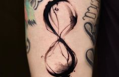 a black and white photo of an hourglass tattoo on the right arm, with ink splatters all over it