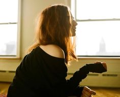 a woman sitting on the floor in front of a window with her hands up to her chest