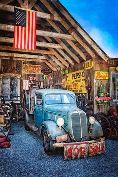 an old blue truck parked in front of a building with american flags on the roof