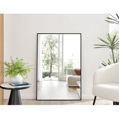 a mirror sitting on top of a wooden floor next to a white chair and potted plant