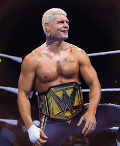 a man with tattoos on his chest standing in front of a ring wearing a wrestling belt