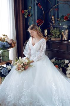 a woman in a white wedding dress sitting on a chair with flowers and greenery