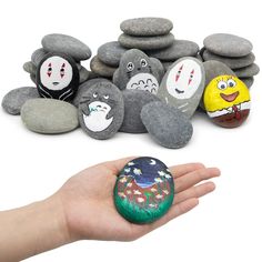 a hand holding some rocks with cartoon faces on them and another rock in the foreground