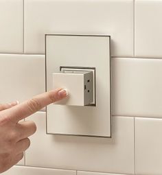 a person is pressing the light switch button on a white tile wall with their finger