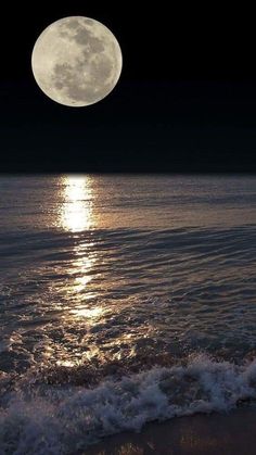 the moon is shining brightly over the water on the beach with waves crashing in front of it