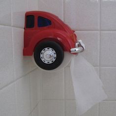 a red toy truck hanging from the side of a white tiled wall with toilet paper