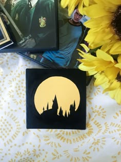 some yellow flowers are sitting on a table with pictures in the background and an image of hogwart's castle