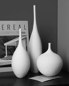 three white vases sitting on top of a table next to a magazine and magazines