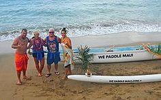 three people standing on the beach next to a surfboard and canoe with palm trees in it